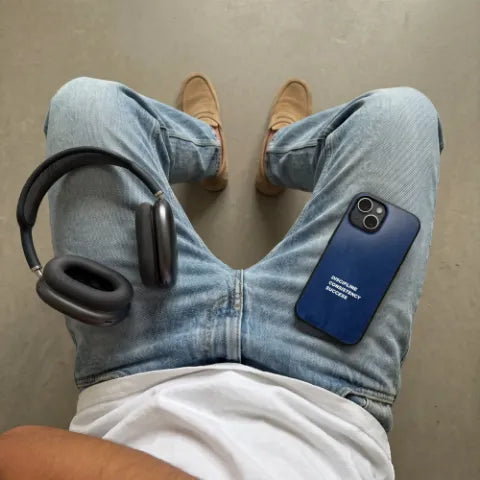 Dunkelblaue Hülle mit weißem Schriftzug auf Jeans, daneben Kopfhörer